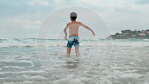 Happy boy having fun at coastline. Carefree guy dancing in water at seashore.