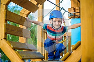 Happy boy having fun and playing at adventure park, holding ropes and climbing wooden stairs