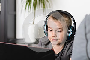 Happy boy in headphones playing online video game on laptop computer at home. Child sitting and use pc