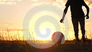 A happy boy hits a soccer ball in slow motion, feeling elated. Silhouette of a child at sunset. Active games, sports.