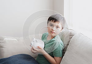 Happy boy holding piggy bank with smiling face. Indoor portrait of a cheerful child showing money saving box.School kid Learning