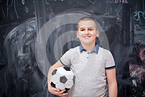 Happy boy holding a soccer ball in front of chalkboard