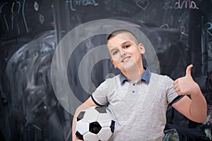 Happy boy holding a soccer ball in front of chalkboard