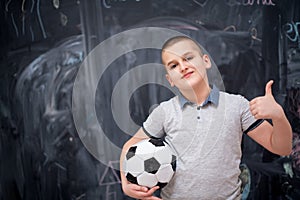 Happy boy holding a soccer ball in front of chalkboard
