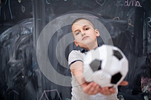 Happy boy holding a soccer ball in front of chalkboard