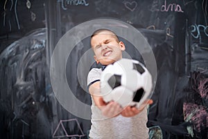 Happy boy holding a soccer ball in front of chalkboard