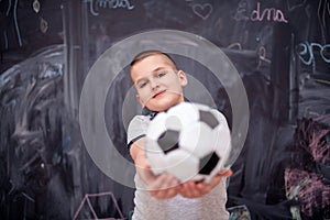 Happy boy holding a soccer ball in front of chalkboard