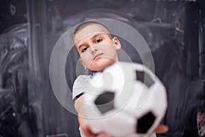 Happy boy holding a soccer ball in front of chalkboard