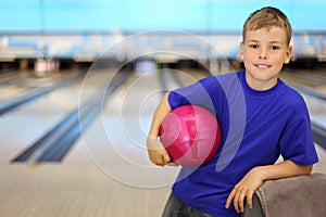 Happy boy holds ball in bowling club