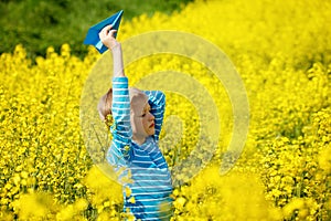 Happy boy holds in hand blue paper airplane on bright sunny day