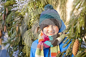 happy boy in a jacket and hat in a winter forest against the background of Christmas trees on a sunny day