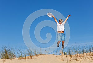 Happy boy jump high on the sand dune holding hat