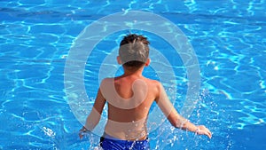 Happy boy jumping into the blue water pool. Slow motion