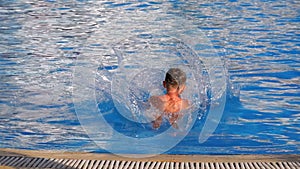 Happy boy jumping into the blue water pool. Slow motion