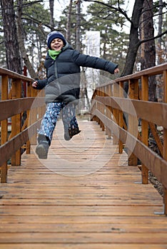 Happy boy jumping and running on a wooden bridge in the forest