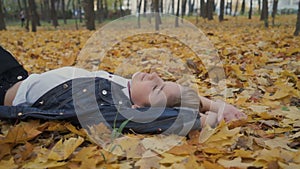 Happy boy lay on autumn leaves in park