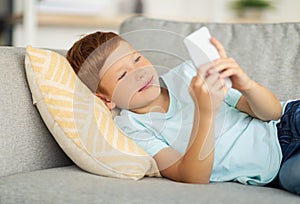 Happy boy laying on couch, using smartphone