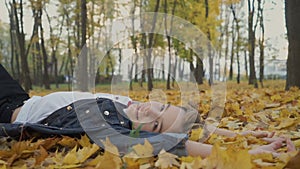 Happy boy lays on yellow leaves in autumn park