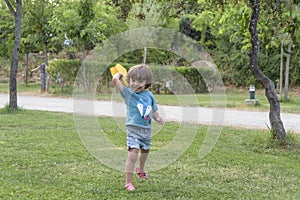 Happy boy leaning and throwing yellow paper airplane on bright sunny day in the field.