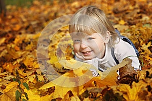 Happy boy in leaves of autumn