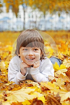 Happy boy in leaves of autumn