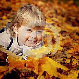 Happy boy in leaves of autumn