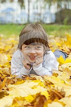 Happy boy in leaves of autumn lies