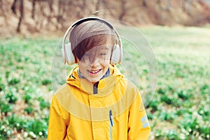 Happy boy listening to music at nature. Kid with headphones relaxing in the spring park