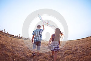 Happy boy and little girl running with bright kite on a meadow