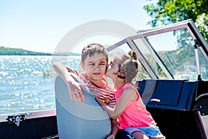 Happy boy and little girl are sitting in a motor boat on the shore of a lake or river. Summer vacation