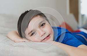 Happy boy lying on sofa looking up at camera with smiling face,Close up face a Child resting in living room with light shining