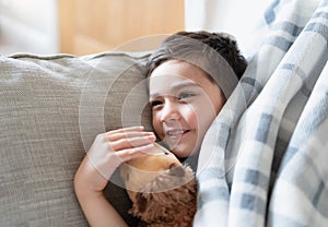 Happy boy lying on sofa relaxing watching TV in morning on early autumn, Comfortable Child laying down on couch with blanket and