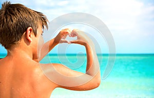 Happy boy making heart with his hands over sea background