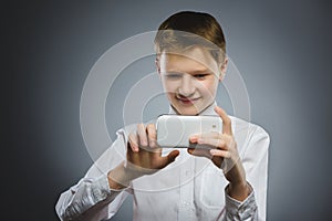 Happy boy with mobile or cell phone making selfie on gray background