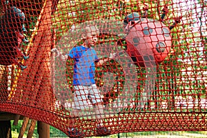 Happy boy overcomes obstacles in rope adventure park. Summer holidays concept. Cute kid playing at rope adventure park. Amusement