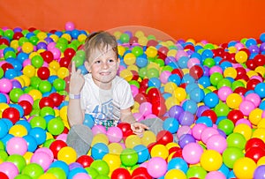 Happy boy playing in ball pit on birthday party in kids amusement park and indoor play center. Child playing with