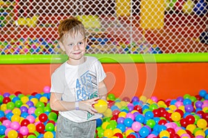 Happy boy playing in ball pit on birthday party in kids amusement park and indoor play center. Child playing with