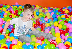 Happy boy playing in ball pit on birthday party in kids amusement park and indoor play center. Child playing with