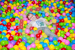 Happy boy playing in ball pit on birthday party in kids amusement park and indoor play center. Child playing with