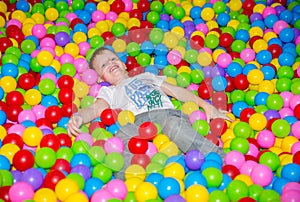 Happy boy playing in ball pit on birthday party in kids amusement park and indoor play center. Child playing with