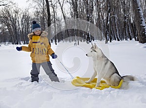 Happy boy playing with dog or husky outdoors in winter day.