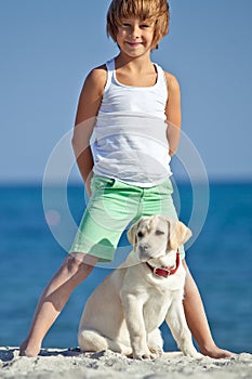 Happy boy playing with his dog on the seashore against the blue sky. Best friends have fun on vacation.