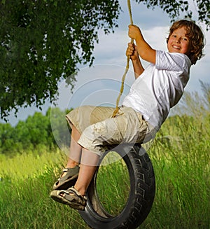 Happy Boy playing on a Swing wheel in the garden. Sunny summer day. activity for kids. child having fun and swinging on car tire