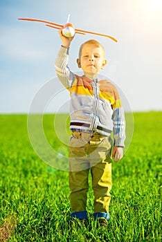 Happy boy playing with toy airplane against blue summer sky and green field background.