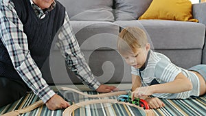 Happy boy playing toy cars with loving grandad moving autos together smiling