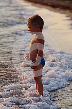 A happy boy is playing in the waves on the beach. Cheerful boy bathes in the sea waves at sunset