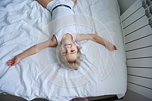 Happy kids playing in white bedroom. Little boy and girl, brother and sister play on the bed wearing pajamas. Family at