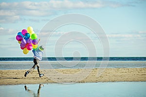 Happy boy plays with colored balloons on the beach