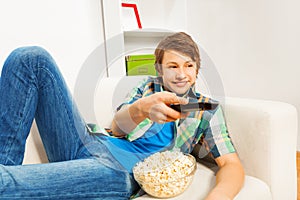 Happy boy with popcorn relaxing on white sofa