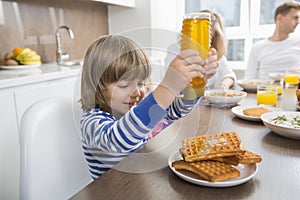 Happy boy pouring honey on waffles while having breakfast with family